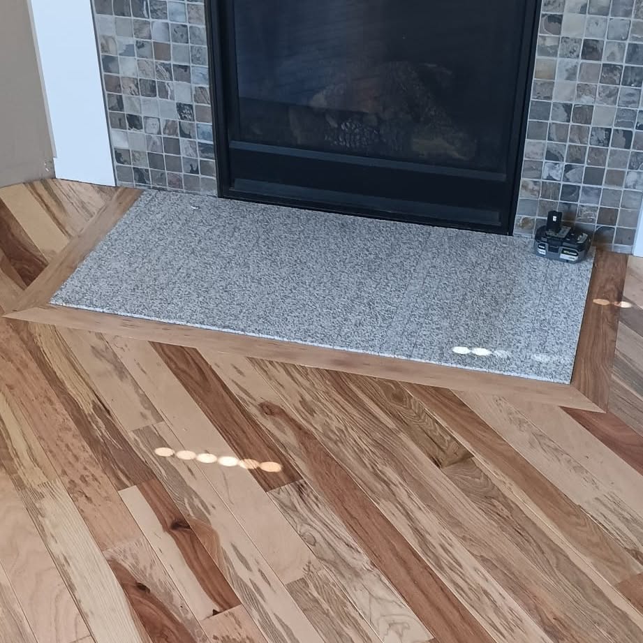 Character hickory hardwood floor with heavy grain variation, meeting a fireplace hearth.